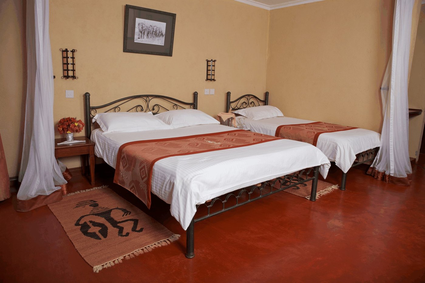 Twin beds with red throws and an African-print rug in a room at Ashnil Aruba Lodge