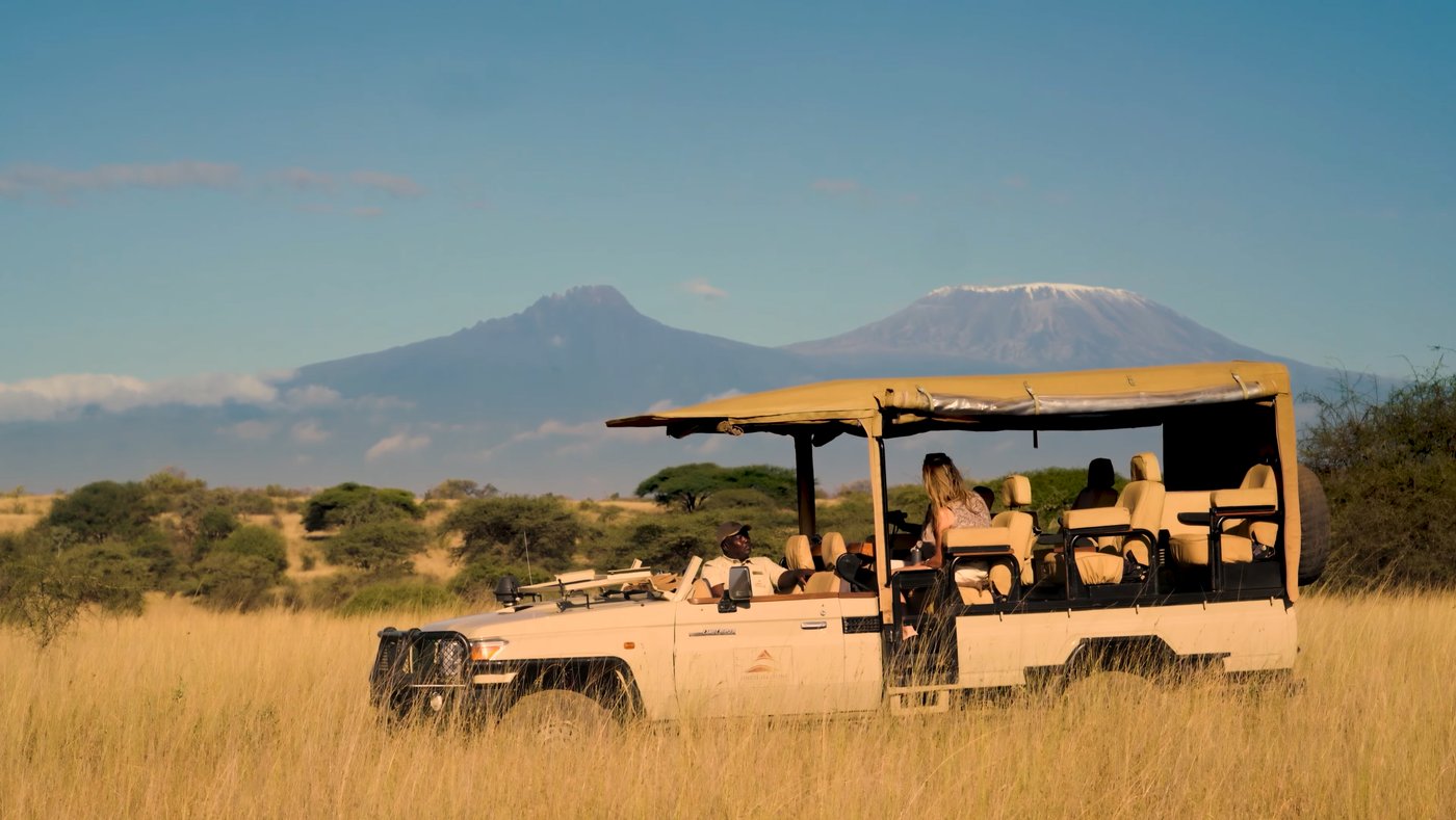 An open Finch Hattons safari vehicle in golden grass with Kilimanjaro behind.