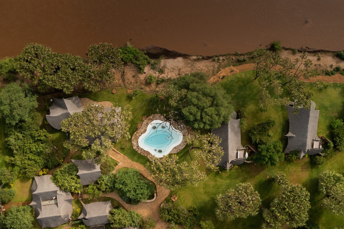 Aerial view shows the pool and thatched cottages beside the river at Galdessa Little in Tsavo