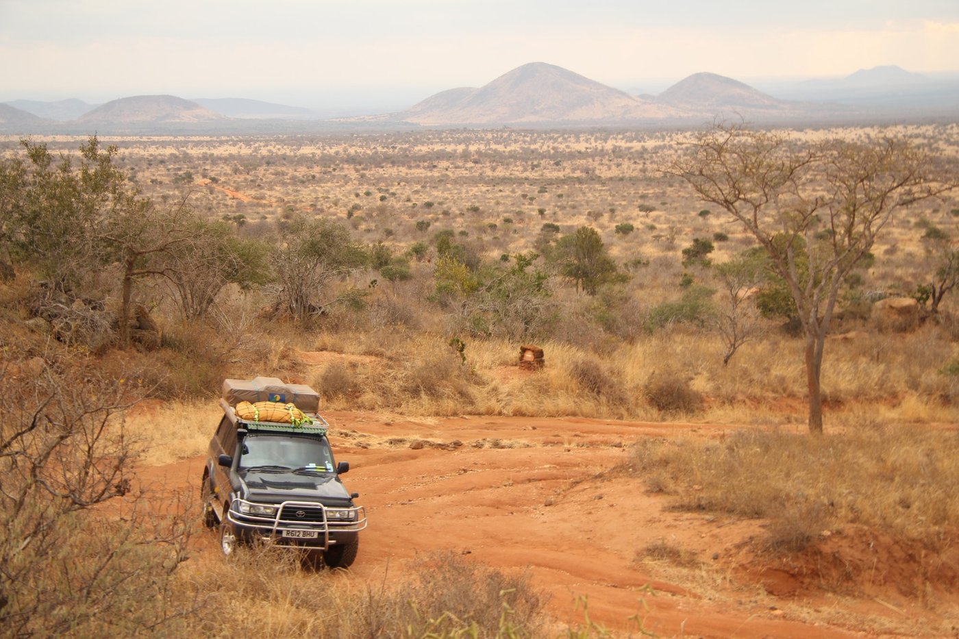 Safari vehicle driving a dirt track through Tsavo West scrubland near Kitani Bandas