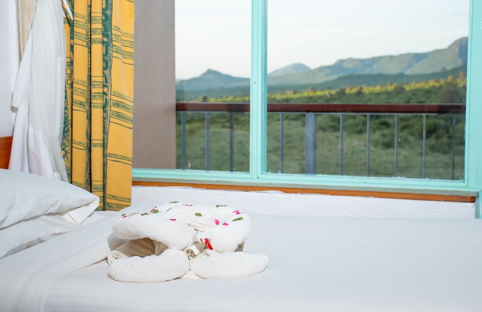 Towel art tops the bed beside a window onto open grassland at Ngulia Safari Lodge