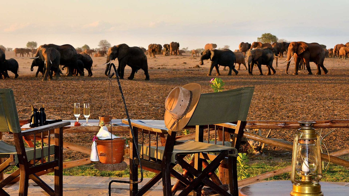 Safari chairs and a table on the viewing balcony at Satao Camp, elephants passing beyond
