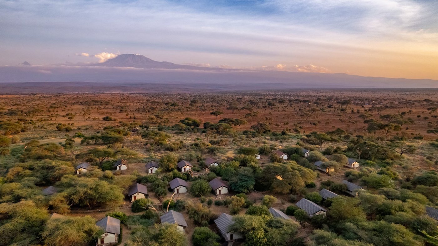 Aerial view over Sentrim Tsavo East Camp shows tents scattered through bush toward distant Kilimanjaro