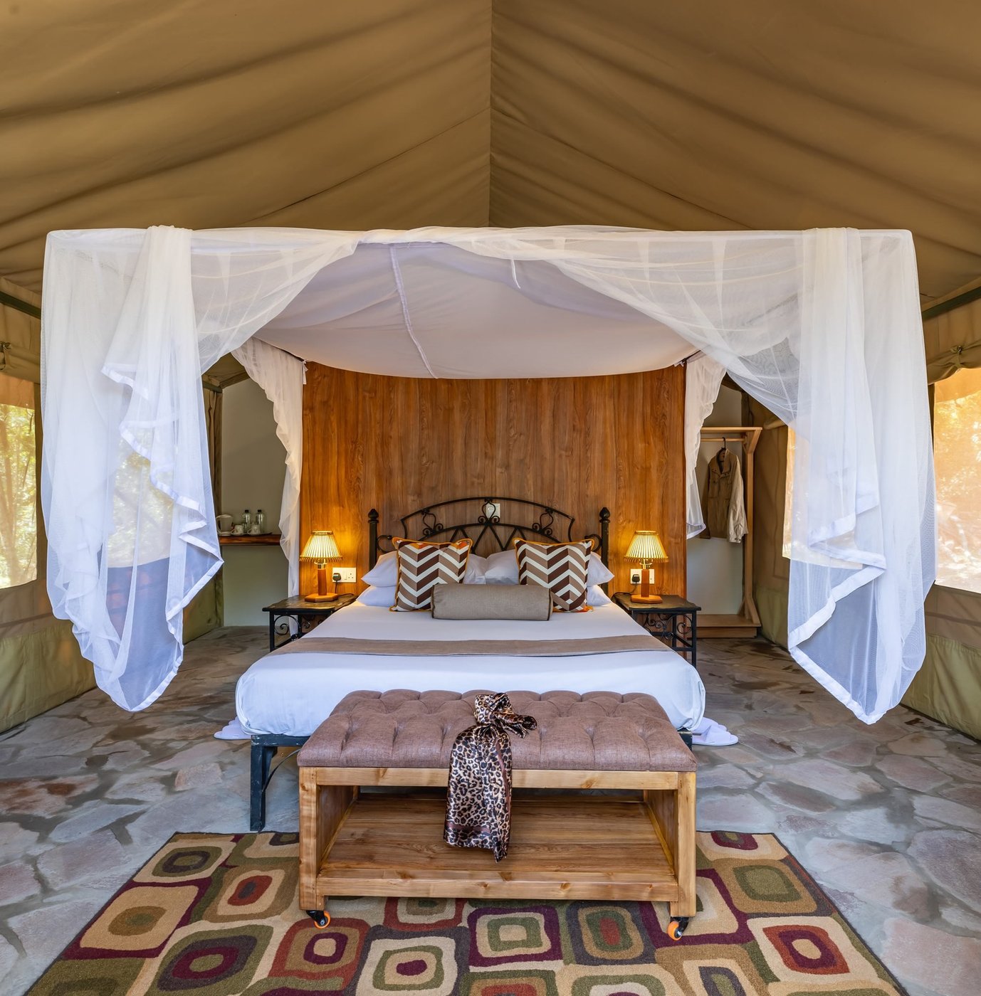 A canopy bed stands draped in white beneath wood beams at Sentrim Tsavo East Camp
