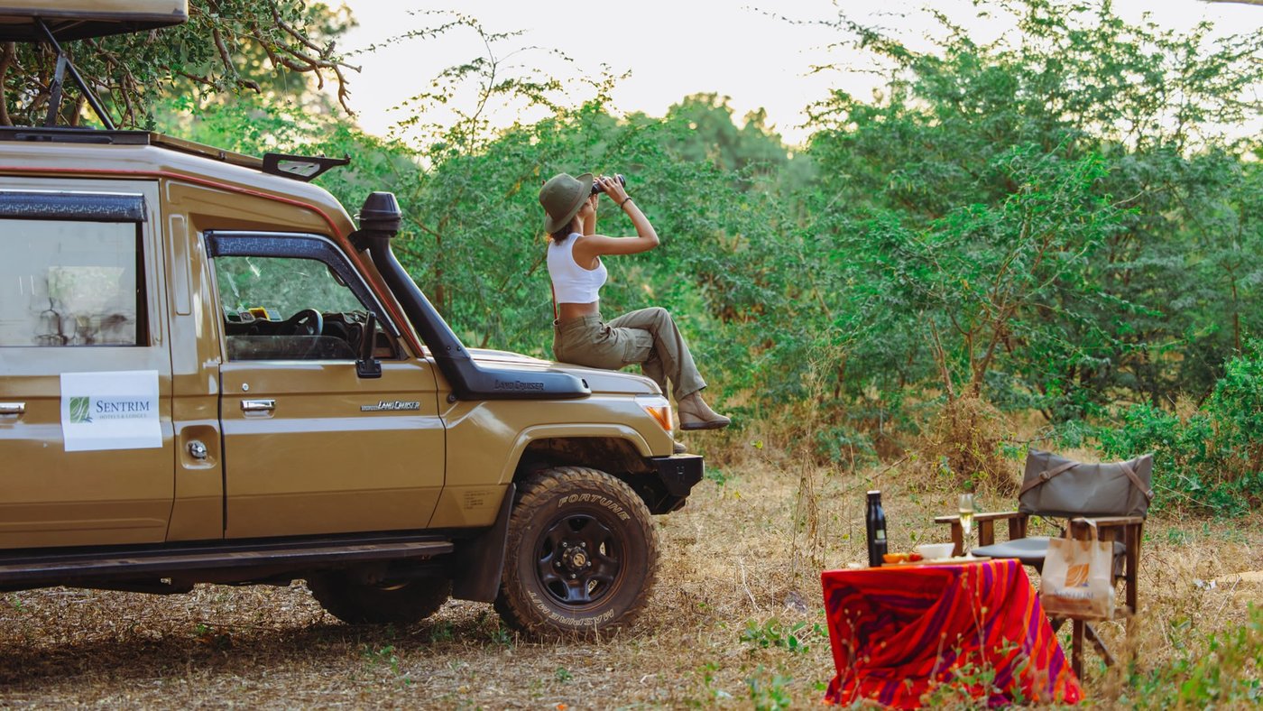 A guest scans the bush with binoculars near a sundowner table at Sentrim Tsavo East Camp