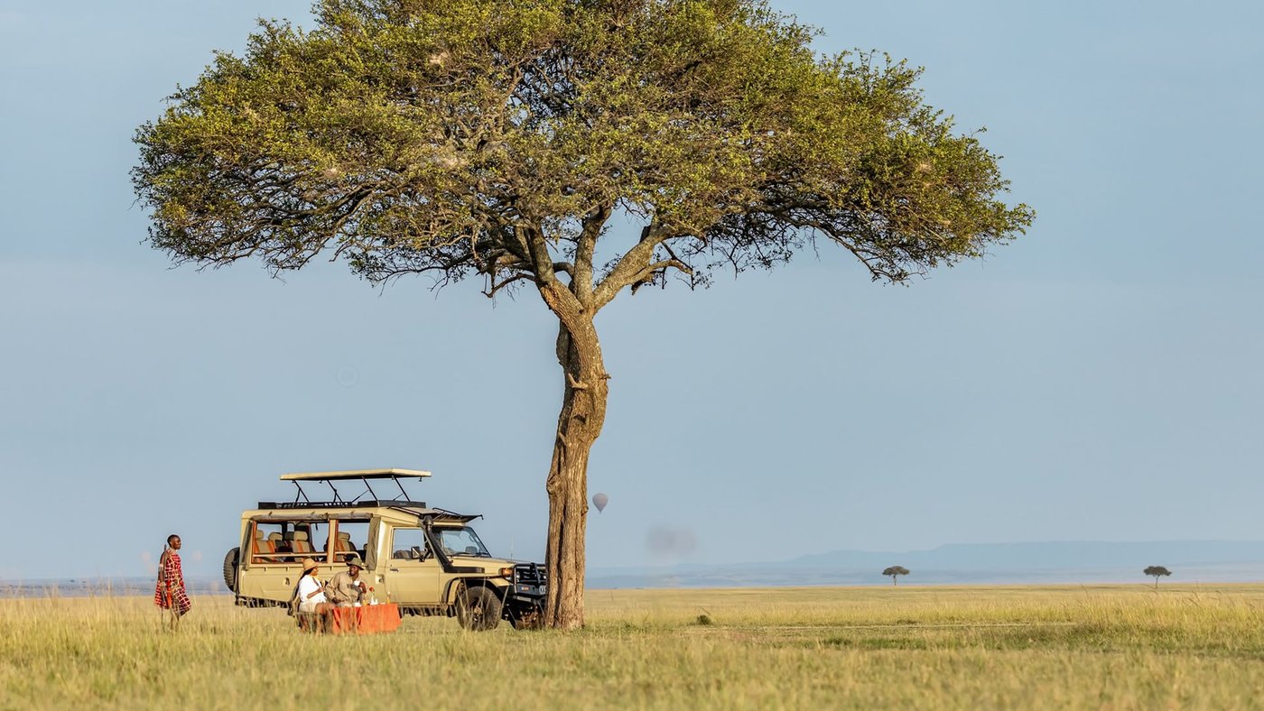 A lone acacia shades a parked safari vehicle on the plain at Sentrim Tsavo East Camp