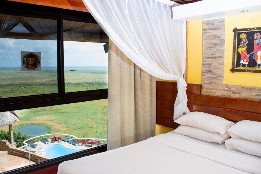 Sheer curtains frame a window over the pool and grassland at Voi Safari Lodge
