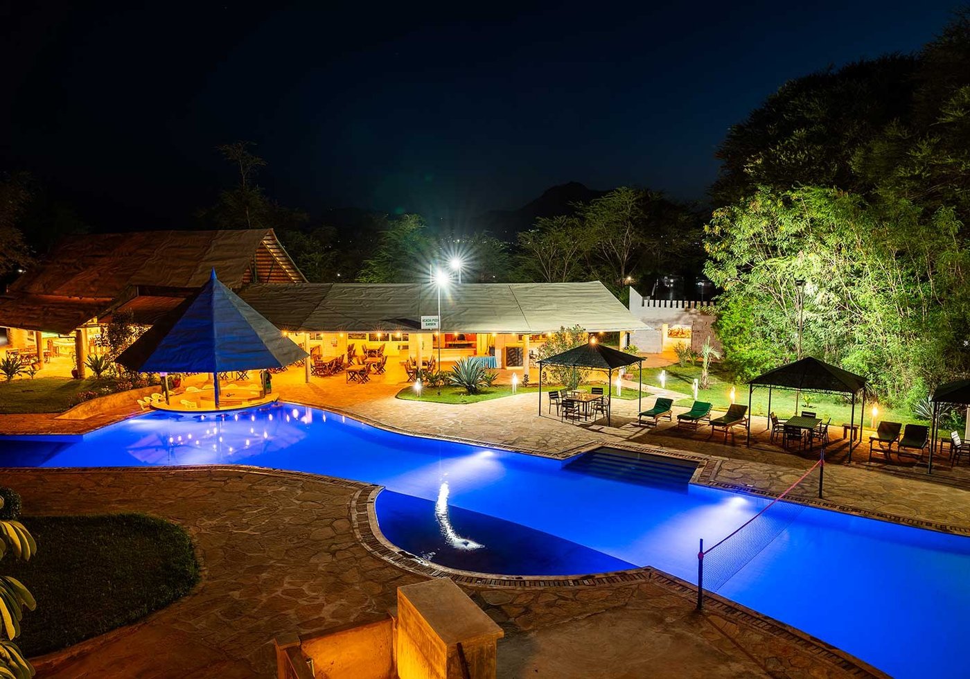 Swimming pool glowing blue at night beside the lit-up lodge buildings at Voi Wildlife Lodge