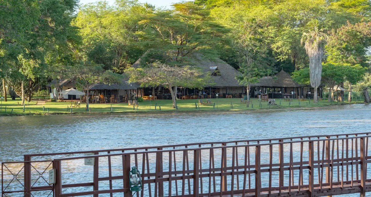 Thatched dining and bar buildings line the lawn above the river at Voyager Ziwani in Tsavo