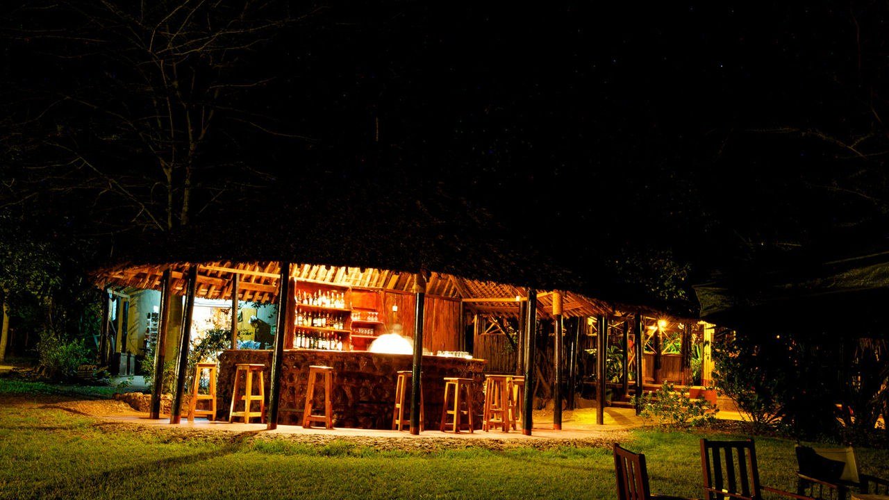 Bar stools and bottles glow beneath a thatched roof at night at Voyager Ziwani