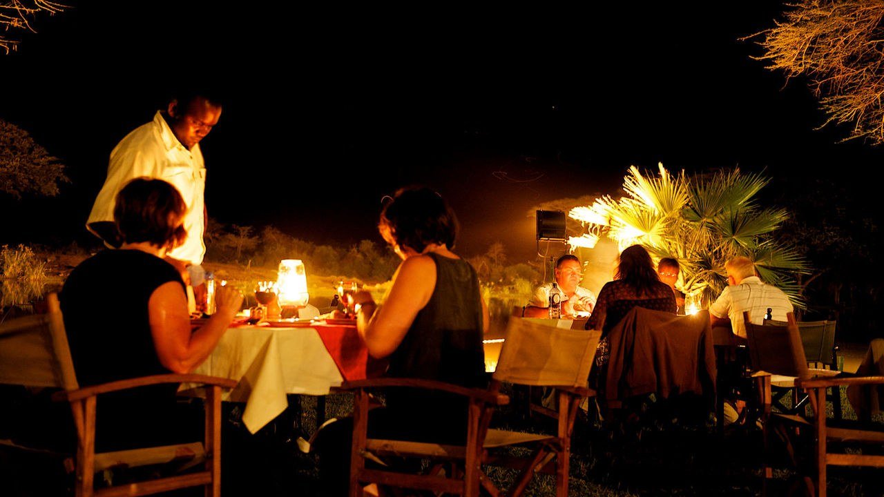 Guests share a candlelit dinner beside the river at Voyager Ziwani