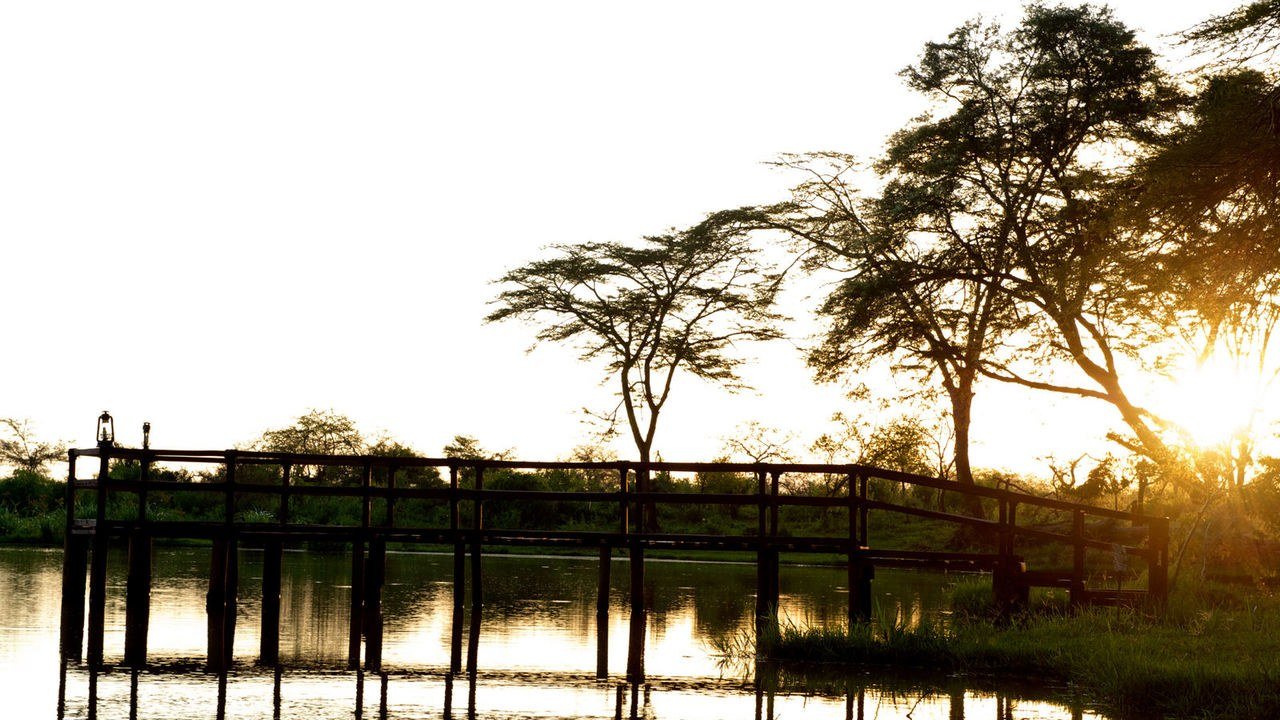 A wooden footbridge crosses the river at sunset at Voyager Ziwani