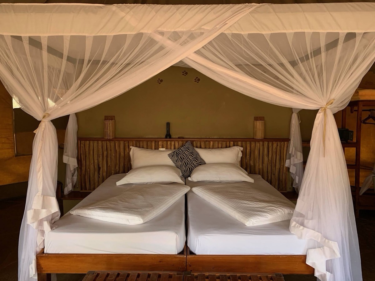 Inside one of the tents: twin beds under a single net, a bamboo headboard, a wardrobe to the right. The net is not decoration. Tsavo is high-risk malaria country all year.